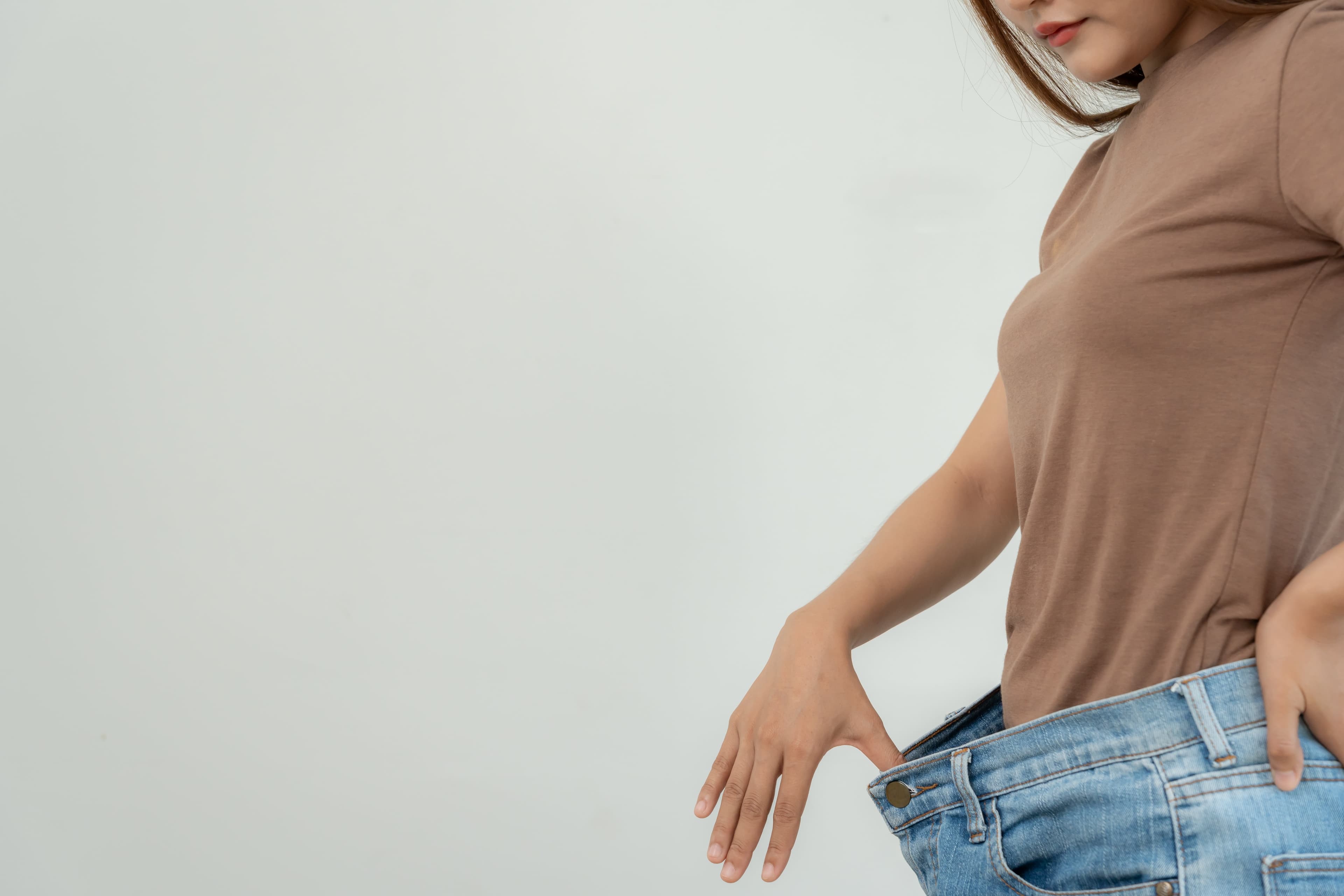 Eine Frau, die ihre weiten Jeans hochhält, weil sie eine beträchtliche Menge an Körpergewicht verloren hat.
